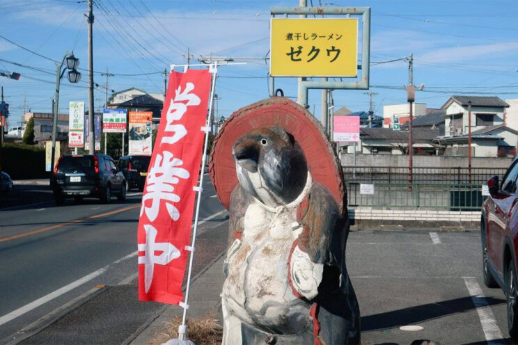 『煮干しラーメンゼクウ』の店舗前の看板とたぬきの陶器